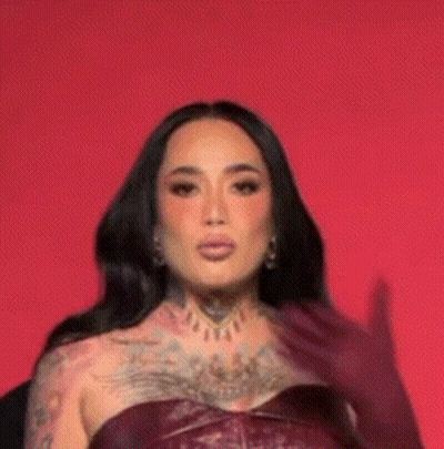 A Woman With A Lot Of Tattoos On Her Body Is Wearing A Burgundy Leather Dress And Gloves . GIF