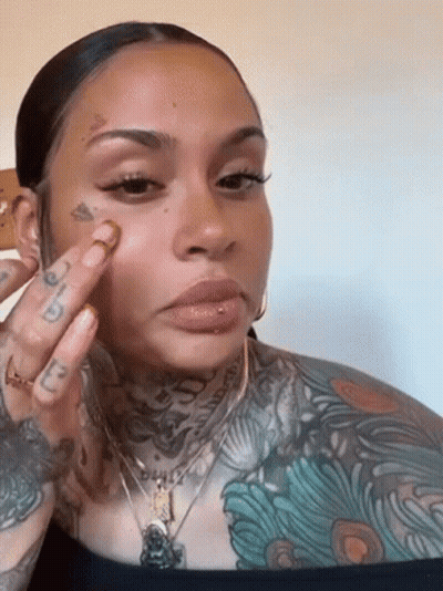 A Woman With A Lot Of Tattoos On Her Face Is Applying Makeup . GIF