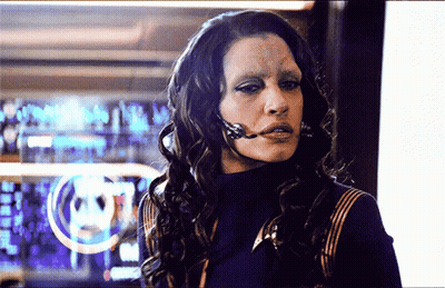 A Woman With A Microphone On Her Face Is Standing In Front Of A Computer Screen GIF