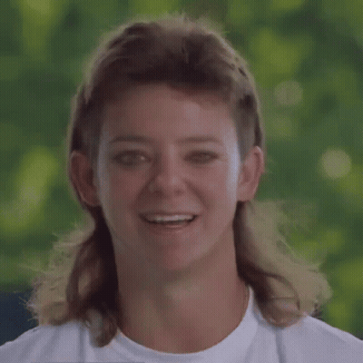 A Woman With A Mullet And A White Shirt Smiles GIF