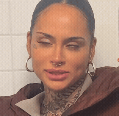 A Woman With A Nose Ring And Tattoos On Her Face Is Taking A Selfie . GIF
