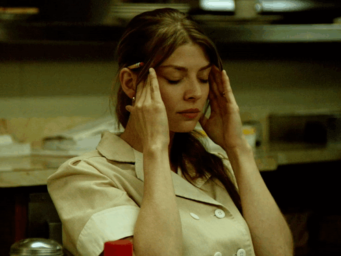 A Woman With A Pencil In Her Hair Holds Her Hands To Her Head GIF