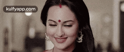 A Woman With A Red Bindi On Her Forehead Is Smiling And Looking Down . GIF