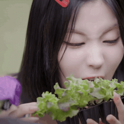 A Woman With A Red Hair Clip Is Eating Lettuce From A Container GIF