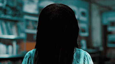 A Woman With A Ring In Her Hair Is Standing In A Library GIF