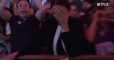 A Woman With A Ring On Her Finger Is Covering Her Mouth In A Crowd Of People With Netflix Written On The Bottom GIF