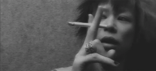 A Woman With A Ring On Her Finger Is Smoking A Cigarette In A Black And White Photo . GIF