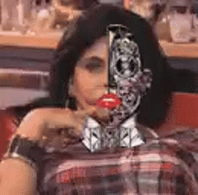 A Woman With A Robot Face On Her Face Is Sitting In A Chair . GIF