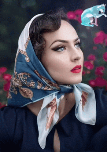 A Woman With A Scarf Around Her Head Has A Blue Cat Flying Above Her Head GIF