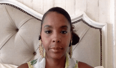 A Woman With A Scarf Around Her Neck Is Sitting In Front Of A Bed GIF