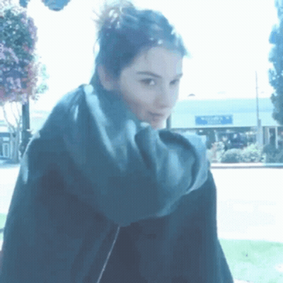 A Woman With A Scarf Around Her Neck Is Standing In Front Of A Building That Says Walmart GIF