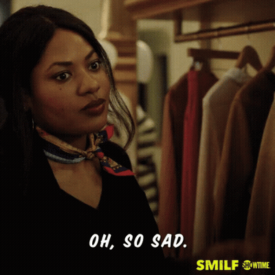 A Woman With A Scarf Around Her Neck Is Standing In Front Of A Closet And Says Oh So Sad GIF