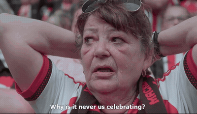 A Woman With A Scarf That Says Mack On It Is Asking Why Is It Never Us Celebrating GIF