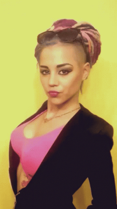 A Woman With A Shaved Head And A Pink Top GIF