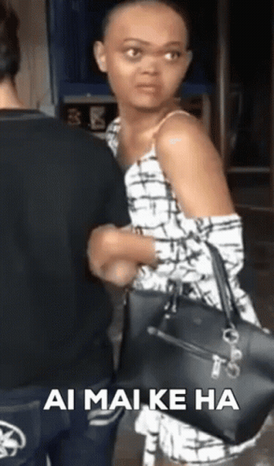 A Woman With A Shaved Head Is Holding A Black Purse While Standing Next To A Man . GIF