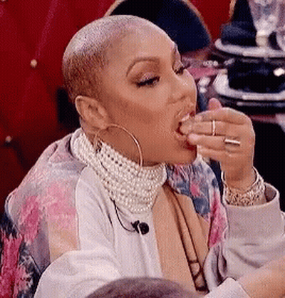 A Woman With A Shaved Head Is Sitting At A Table Eating Food . GIF