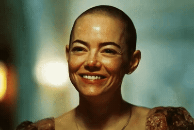 A Woman With A Shaved Head Is Smiling In A Dark Room . GIF