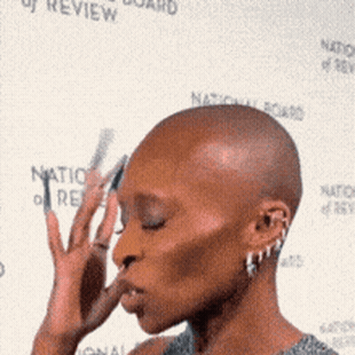 A Woman With A Shaved Head Is Standing In Front Of A National Board Of Review Banner GIF