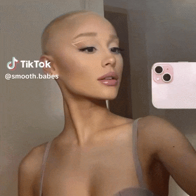 A Woman With A Shaved Head Is Taking A Selfie In Front Of A Pink Phone . GIF