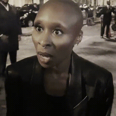 A Woman With A Shaved Head Is Wearing A Black Jacket And Earrings . GIF