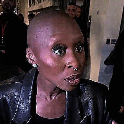 A Woman With A Shaved Head Is Wearing A Leather Jacket And Earrings . GIF