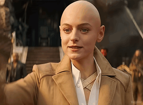 A Woman With A Shaved Head Is Wearing A Tan Jacket And White Shirt GIF