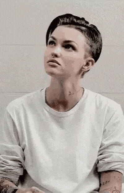 A Woman With A Shaved Head Is Wearing A White Shirt . GIF
