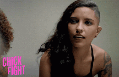 A Woman With A Shaved Head Stands In Front Of A Sign That Says " Chick Fight " GIF