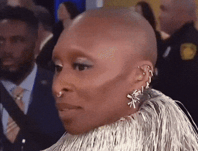 A Woman With A Shaved Head Wearing Earrings And A Fur Coat GIF