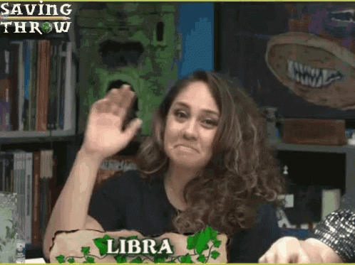 A Woman With A Sign That Says Libra Waves Her Hand GIF