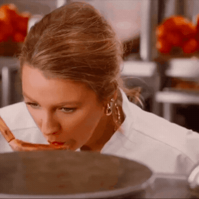 A Woman With A Spoon In Her Mouth Looks At Something In A Pot GIF