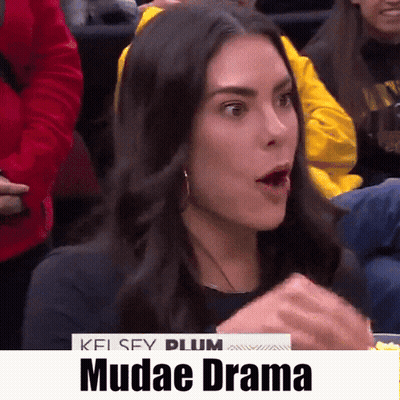 A Woman With A Surprised Look On Her Face Is Sitting In A Crowd With The Words Mudae Drama On The Bottom GIF