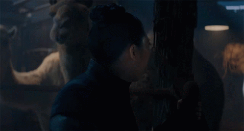 A Woman With A Surprised Look On Her Face Is Standing In A Dark Room With A Statue In The Background GIF