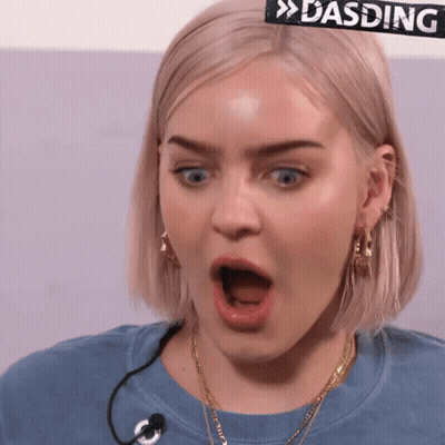 A Woman With A Surprised Look On Her Face Is Wearing A Blue Shirt With A Microphone . GIF