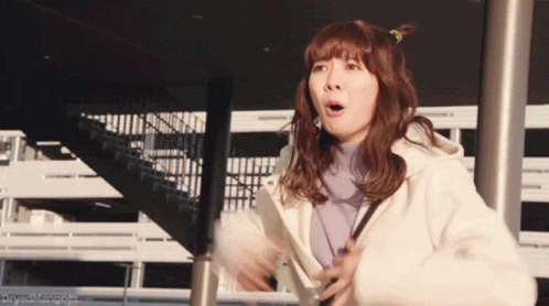 A Woman With A Surprised Look On Her Face Stands In Front Of Stairs GIF