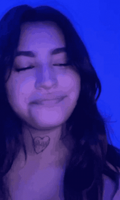 A Woman With A Tattoo Of A Heart On Her Neck Is Smiling With Her Eyes Closed . GIF