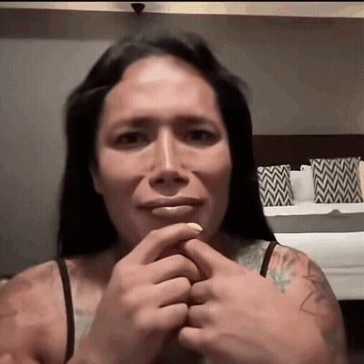 A Woman With A Tattoo On Her Arm Holds Her Hands To Her Face GIF