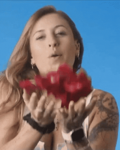 A Woman With A Tattoo On Her Arm Is Blowing Red Roses Into The Air GIF