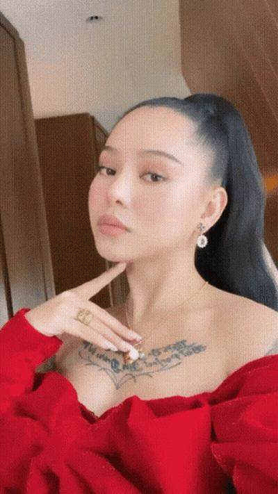 A Woman With A Tattoo On Her Chest Is Wearing A Red Top And Earrings GIF