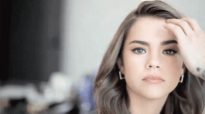 A Woman With A Tattoo On Her Wrist Is Touching Her Hair And Looking At The Camera . GIF
