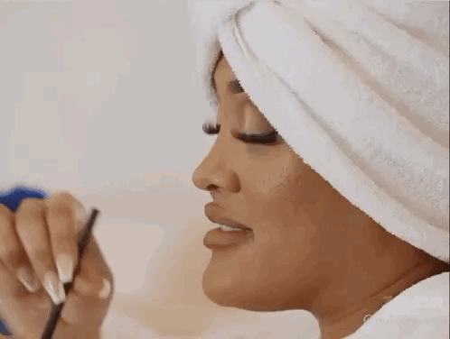 A Woman With A Towel Wrapped Around Her Head Is Applying Makeup To Her Face . GIF