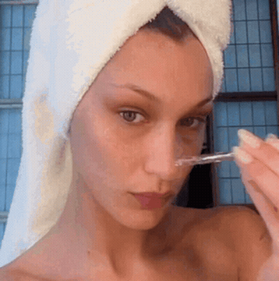 A Woman With A Towel Wrapped Around Her Head Is Using A Pipette To Apply A Product To Her Face . GIF