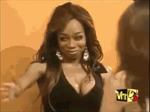 A Woman With A Very Large Breast Is Standing In Front Of A Sign That Says Vh1 . GIF