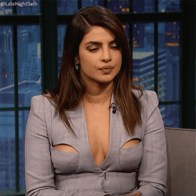 A Woman With A Very Plunging Neckline Is Sitting In A Chair With Her Hands On Her Hips . GIF