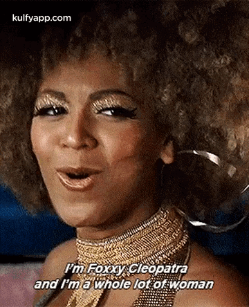 A Woman With An Afro Is Wearing A Gold Necklace And Earrings And Is Talking . GIF