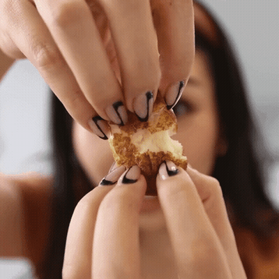 a woman with black and white nails holds a piece of food in her hands