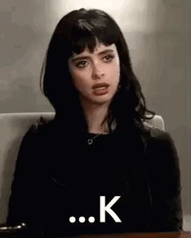 A Woman With Black Hair And Bangs Is Sitting At A Table . GIF
