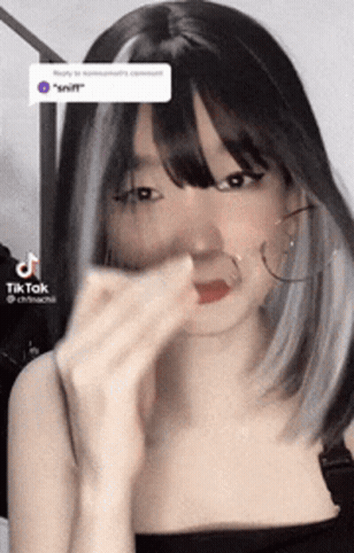 A Woman With Black Hair And Gray Highlights Is Wearing Hoop Earrings And A Black Top . GIF