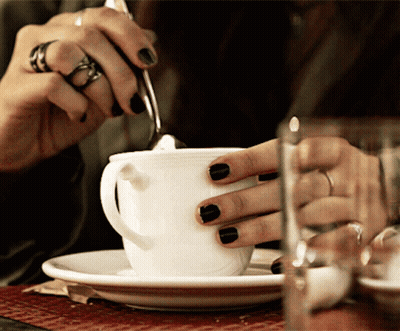 A Woman With Black Nail Polish Is Stirring A Cup Of Coffee GIF