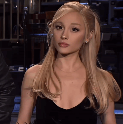 A Woman With Blonde Hair And A Black Dress Looks At The Camera GIF